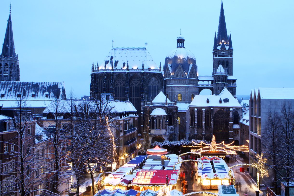 Weihnachtsmarkt vor dem verschneiten Aachener Dom in der Dämmerung